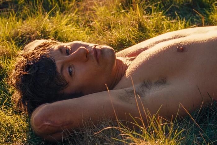 Barry Keoghan lies on the grass shirtless in Saltburn.